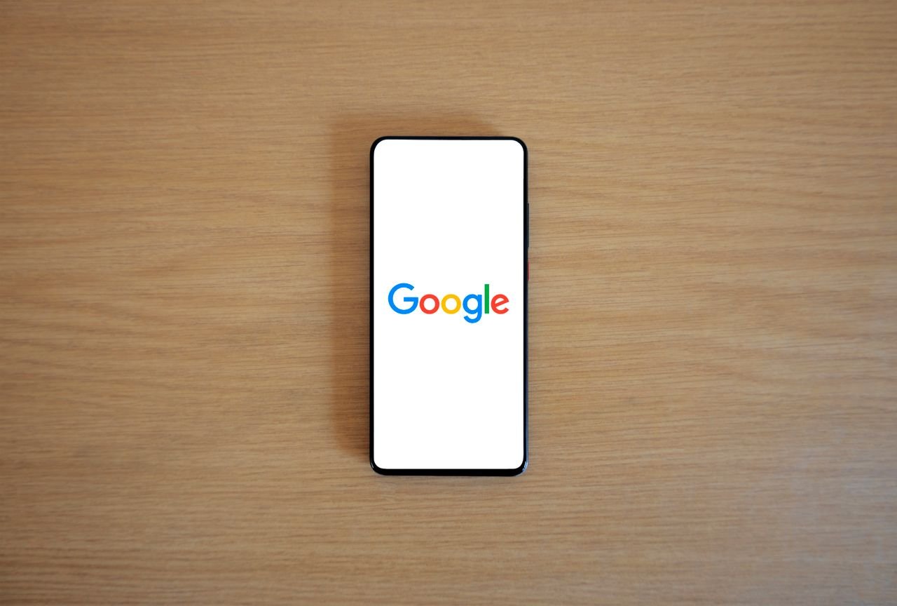 about-us-01 A smartphone displaying the Google homepage on a wooden surface, viewed from above.